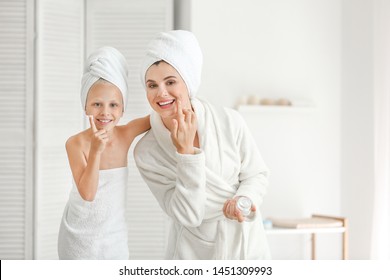 Mother And Little Daughter Applying Cream Onto Face In Bathroom