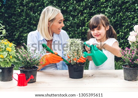 Mother with little daughter having fun and planting flowers in pot with soil together,daughter taking care of flower with watering plants in garden at home