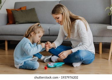 Mother and little daughter paint their nails with toy nail polish. Kid playing with mom at home. Concept of good parenting and happy childhood, family leisure - Powered by Shutterstock