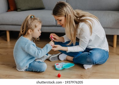 Mother and little daughter paint their nails with toy nail polish. Kid playing with mom at home. Concept of good parenting and happy childhood, family leisure - Powered by Shutterstock