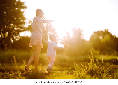 Mother and little daughter playing together in a summer park at sunset. Happy mom with small child  having fun on sunny field. Kisses and hugs. The concept of a happy family. 