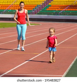 Mother & Little Daughter Running Around The Stadium. Child Runs Away From Mom At The Stadium.