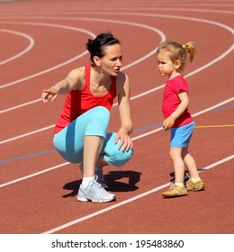 Mother & Little Daughter Running Around The Stadium. Child Runs Away From Mom At The Stadium.