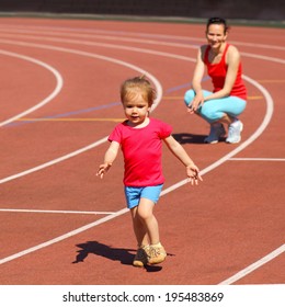 Mother & Little Daughter Running Around The Stadium. Child Runs Away From Mom At The Stadium.