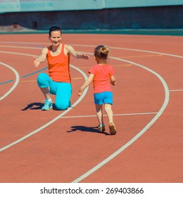 Mother & Little Daughter Running Around The Stadium. Child Runs Away From Mom At The Stadium.