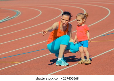 Mother & Little Daughter Running Around The Stadium. Child Runs Away From Mom At The Stadium.