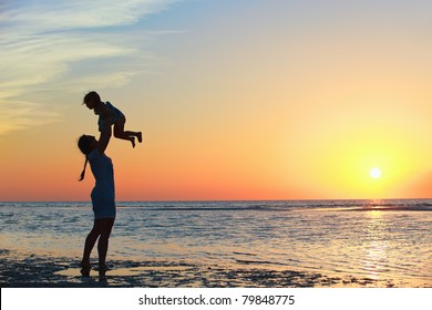 Mother And Little Daughter Silhouettes On Beach At Sunset