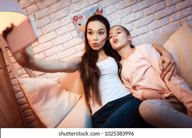 Mother And Little Daughter Taking Selfie On Phone At Night At Home.