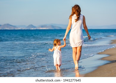 Mother and little daughter walking on the sea beach in Greece