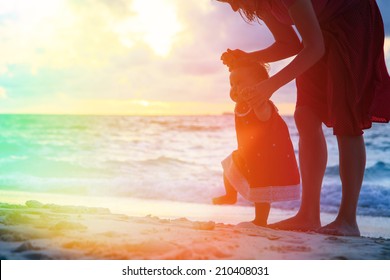 Mother And Little Daughter Walking On Sand Beach At Sunset