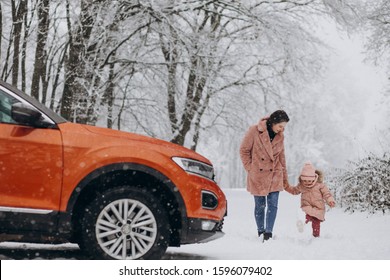 Mother with little daughter in a winter park by car