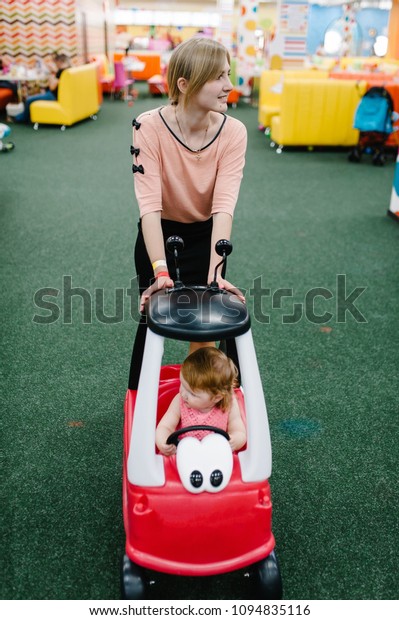 Mother and\
little kids the girl child rides on a red gorgeous big car on the\
road. Close up. The baby is driving the car and played in a\
children\'s playroom on a birthday\
party.