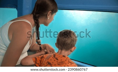 Mother with little son exploring underwater sea world and fishes while traveling on tourist submarine. Holiday, summer vacation and tourism.