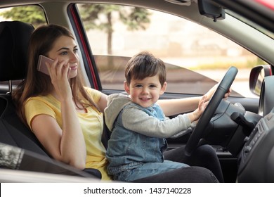 Mother With Little Son On Knees Driving Car And Talking By Phone. Child In Danger