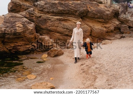 Mother and little son spend time outdoors in the summer or autumn together, sitting on beach.Young mother plays with her baby on the promenade. Summer vacation for two by the sea