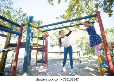 Mother Looking At Daughter Hanging On Jungle Gym At Playground