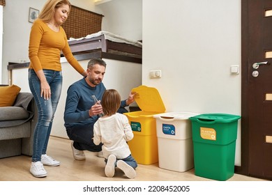 Mother Looking At Father Teaching Little Son Throwing Bottle In Dustbin For Glass At Home. Ecological Garbage Recycle. Parenting. Young Caucasian Family Spending Time Together. Domestic Lifestyle