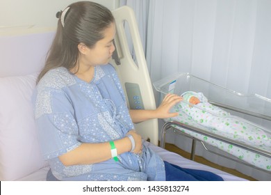Mother looks at her newborn baby in bed immediately after a birth labour. Concept photo of pregnant woman, newborn, baby, pregnancy.