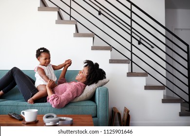 Mother Lying On Sofa At Home Playing With Baby Daughter