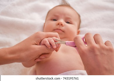 Mother Make Manicure With Nail Clippers And Cutting Nails Her Cute Baby While Laying On The Bed. Concept Of Baby Care