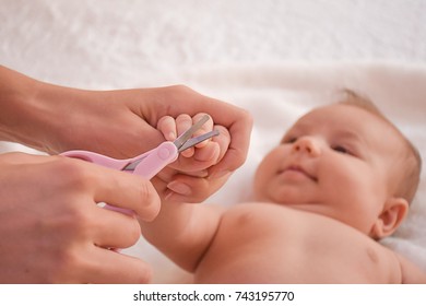 Mother Make Manicure With Nail Clippers And Cutting Nails Her Cute Baby While Laying On The Bed. Concept Of Baby Care