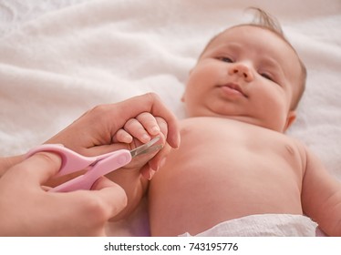 Mother Make Manicure With Nail Clippers And Cutting Nails Her Cute Baby While Laying On The Bed. Concept Of Baby Care