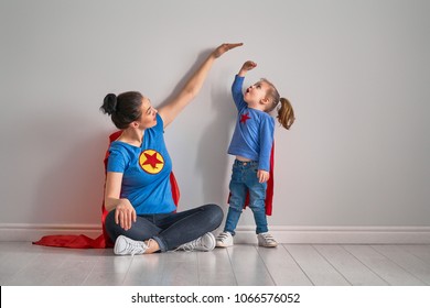 Mother is measuring growth of child daughter near empty wall. Girl in superhero costume.