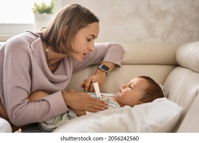 Mother Measuring Temperature Of Her Ill Kid At Background. Sick Child With High Fever Lying At Sofa At Home. High Quality 4k Footage