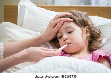 Mother measuring temperature of her ill kid. Sick child with high fever laying in bed and mother holding thermometer. Hand on forehead.  - Powered by Shutterstock