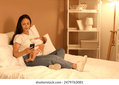 Mother with mobile phone breastfeeding her baby on bed at night - Powered by Shutterstock