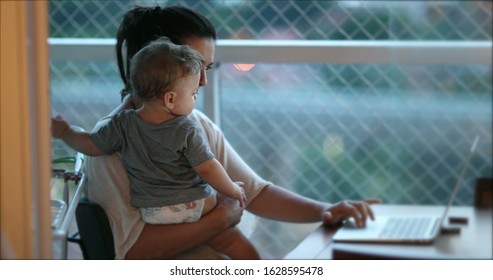 
Mother Multi-tasking, Holding Baby Infant And Using Computer Laptop At Home. Candid Authentic And Real Life Mom Working And Parenting