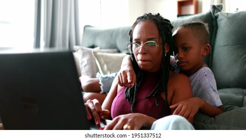 Mother multi-tasking using computer laptop at home. Candid authentic and real life mom working and parenting