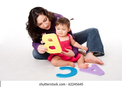 Mother, nanny, or teacher teaching happy baby to learn alphabet, A, B, C, with letters in a playful way, while sitting on floor.