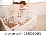 Mother near her cute little sleeping baby in crib at home