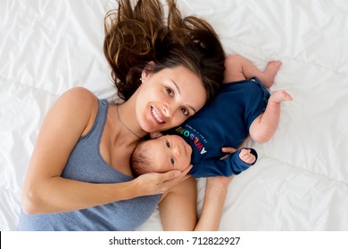 Mother and newborn baby boy, lying in bed, hugging with love, high angle shot, from above. Happy family concept