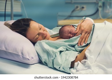 Mother and newborn. Child birth in maternity hospital. Young mom hugging her newborn baby after delivery. Woman giving birth. First moments of baby life after labor. - Shutterstock ID 1942308784