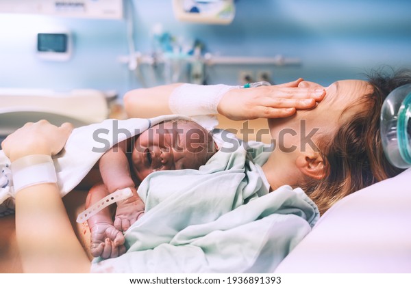 Mother and newborn. Child birth\
in maternity hospital. Young mom hugging her newborn baby after\
delivery. Woman giving birth. First moments of baby life after\
labor.
