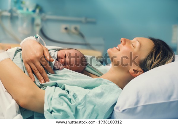 Mother and newborn. Child birth\
in maternity hospital. Young mom hugging her newborn baby after\
delivery. Woman giving birth. First moments of baby life after\
labor.