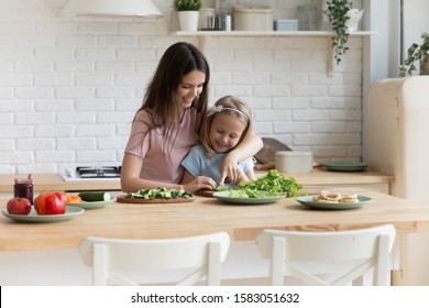 mother or older sister teaches little kid daughter or younger sister how cook vegetable salad holding knife cutting lettuce leaf explain preparing dinner together with small helper in domestic kitchen - Powered by Shutterstock