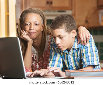Mother overlooks as her teenaged son uses his laptop to study in their kitchen
