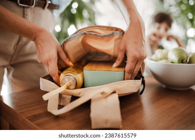 Mother packing school bag for kid. Putting bottle of juice, snacks for children into school bag. Snack, school lunch in a snack box for school. - Powered by Shutterstock