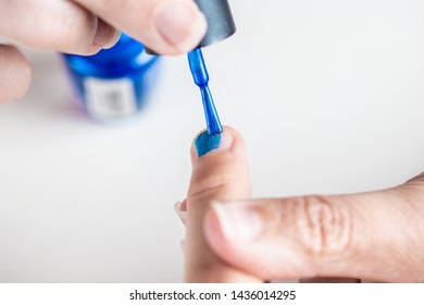 A Mother Paints Her Young Girl's Hands With Blue And Pink Nailpolish, Viewed Against An Isolated White Background