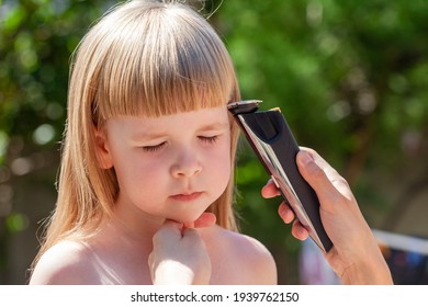 Mother, Parent Cutting Her Young Little Daughter's Hair Using An Electric Hair Trimmer, Outdoors Portrait. Electrical Hair Clipper Amateur Haircut At Home Simple Concept, Lifestyle Shot, Face Closeup