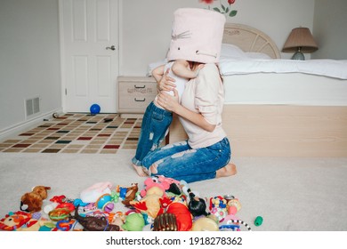 Mother Parent Playing With Baby Toddler In Bedroom. Mom And Kid Boy Girl With Toy Bin On Heads. Family Having Fun At Home. Candid Authentic Happy Childhood Lifestyle. Family Life With Kids. 