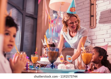 Mother At Party. Kind Loving Mother Smiling Happily And Feeling Happy While Putting Birthday Cake On The Party Table