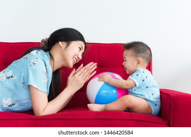 Mother Play With Her 8 Month Old Son In Blue Dress On Red Sofa Bed