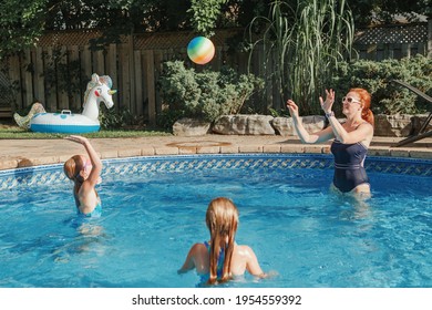 Mother Playing Ball With Daughters Children In Swimming Pool On Home Backyard. Mom And Sisters Siblings Having Fun In Swimming Pool Together. Summer Outdoors Water Activity For Family And Kids. 