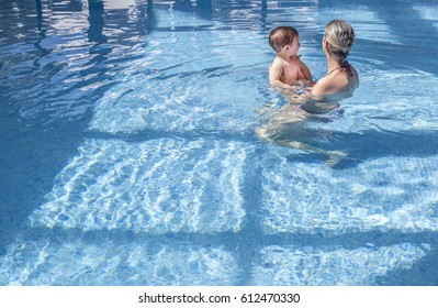 Mother Playing With Her Baby At Swimming Pool Indoor. Kids Learn To Swim During Family Vacation