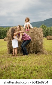 Mother Playing Outdoors With Her Daughters Lifting Them On Top Of A Haystack