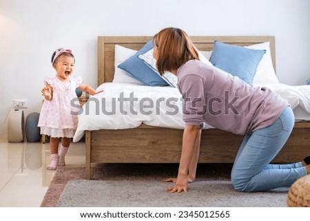 Mother is playing peek a boo or hide and seek with her little baby toddler in the bedroom while the girl is laughing in happiness for good parenting and healthy raising kid